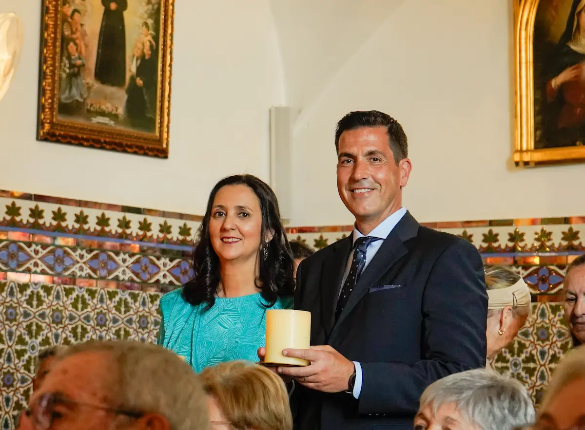 Padres sosteniendo la vela bautismal y sonriendo a cámara en la iglesia