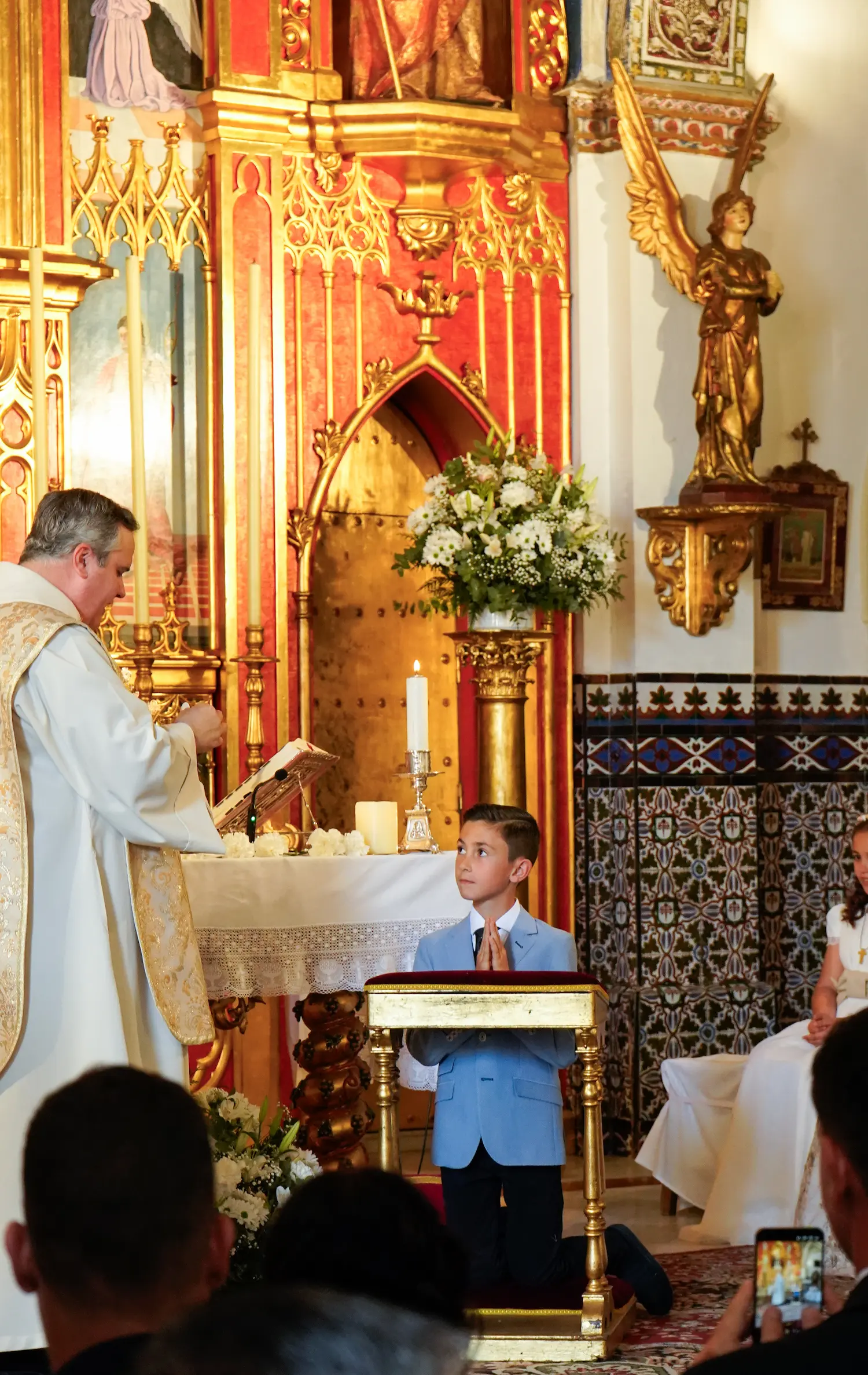 Sacerdote bendiciendo a un niño arrodillado durante la ceremonia religiosa de su primera comunión