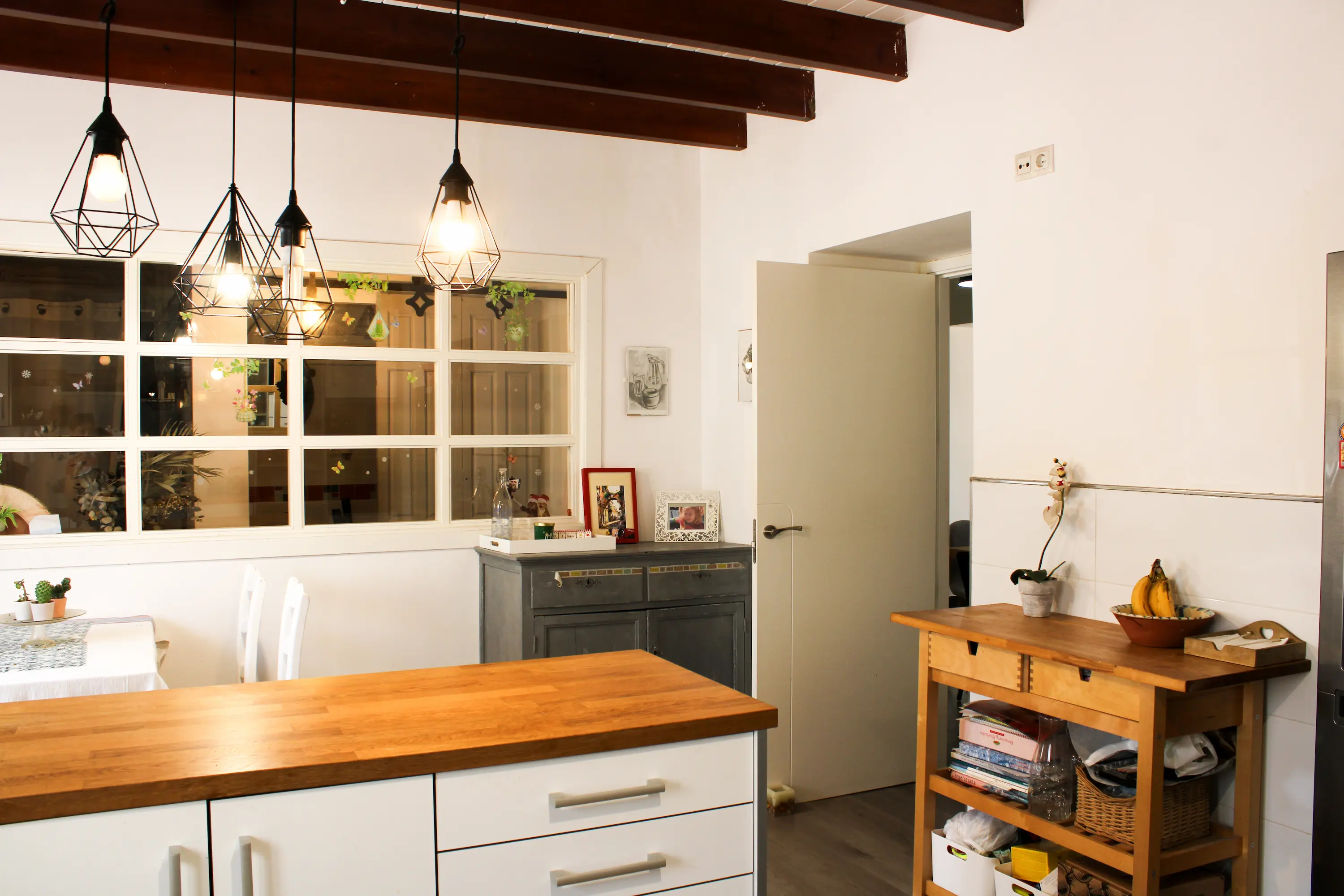Living room with exposed wooden ceiling beams, hanging lamps, matching white furniture, and an interior window