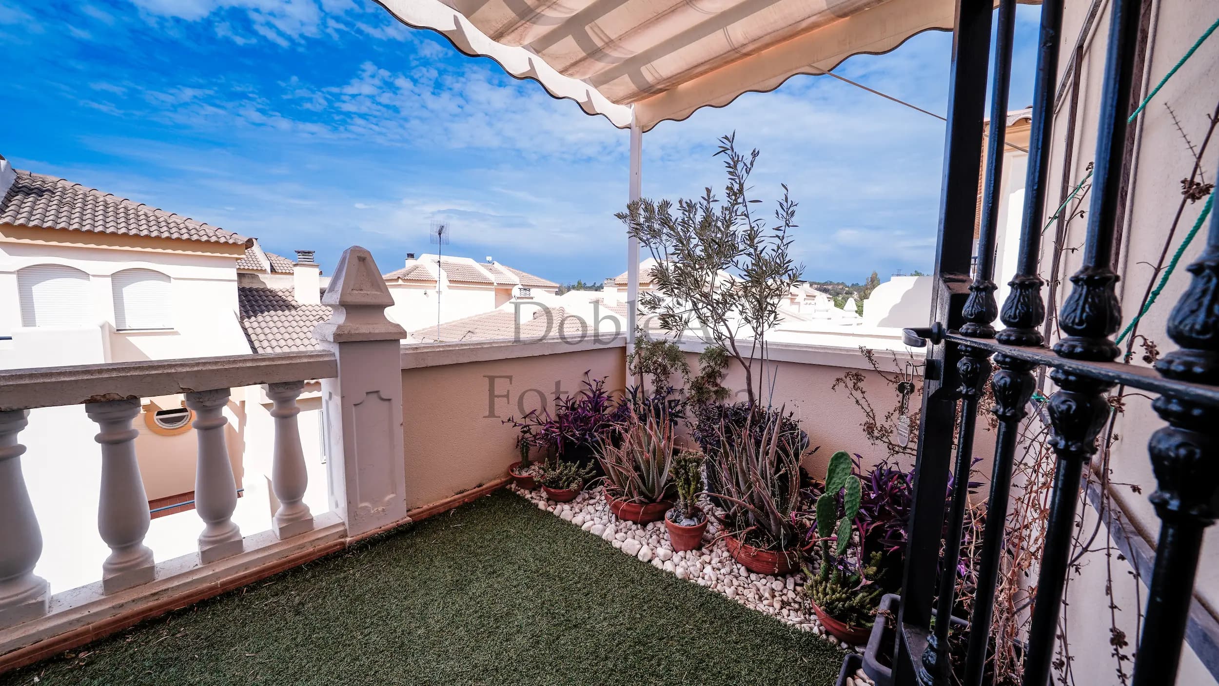 Image of a modern terrace with artificial grass, white stone garden, and potted plants under a blue sky