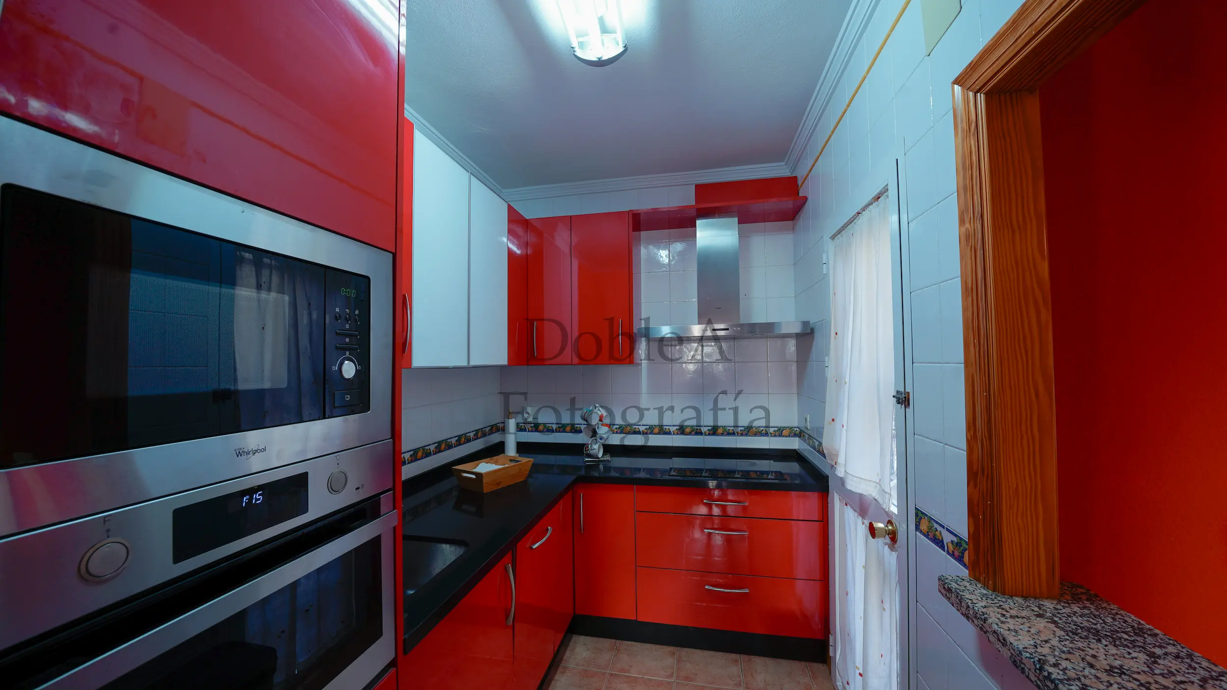 Interior photograph of a modern kitchen with a black countertop, red cabinets, and a serving hatch window connected to the living room