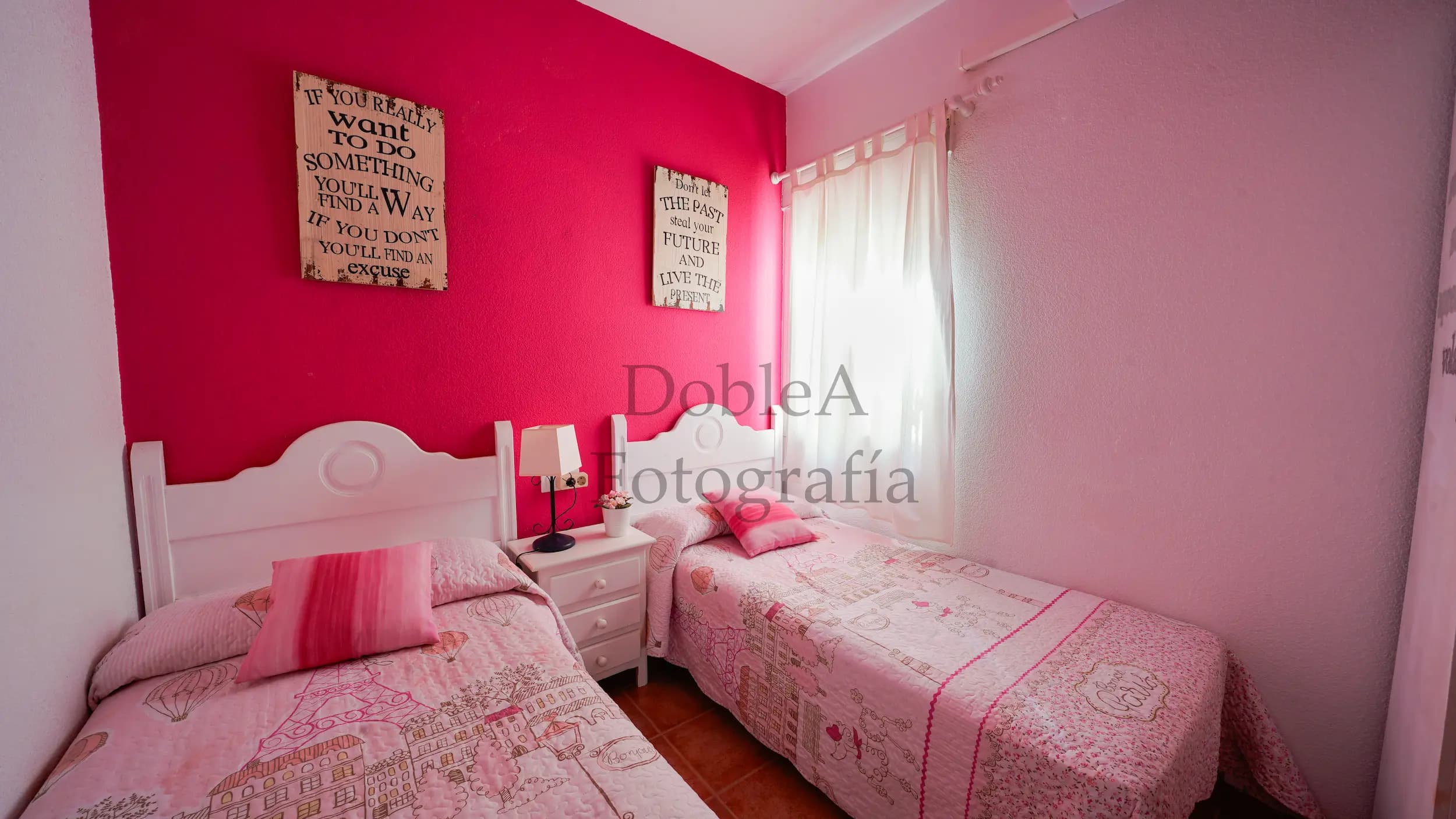 Real estate photograph of a bright bedroom with pink walls and two twin beds