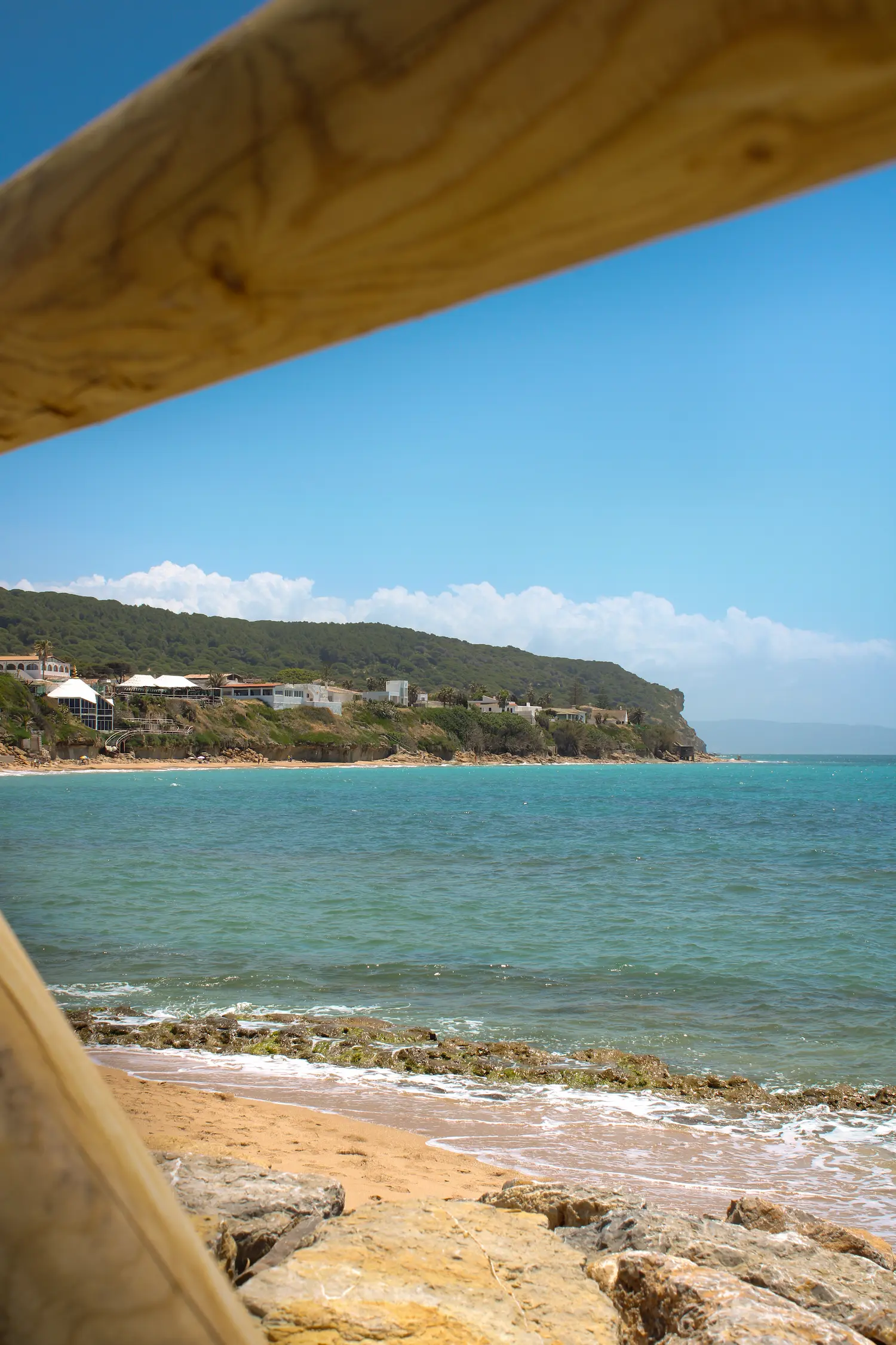 Paisaje costero enmarcado por una valla de madera rústica con vistas al mar y a la montaña
