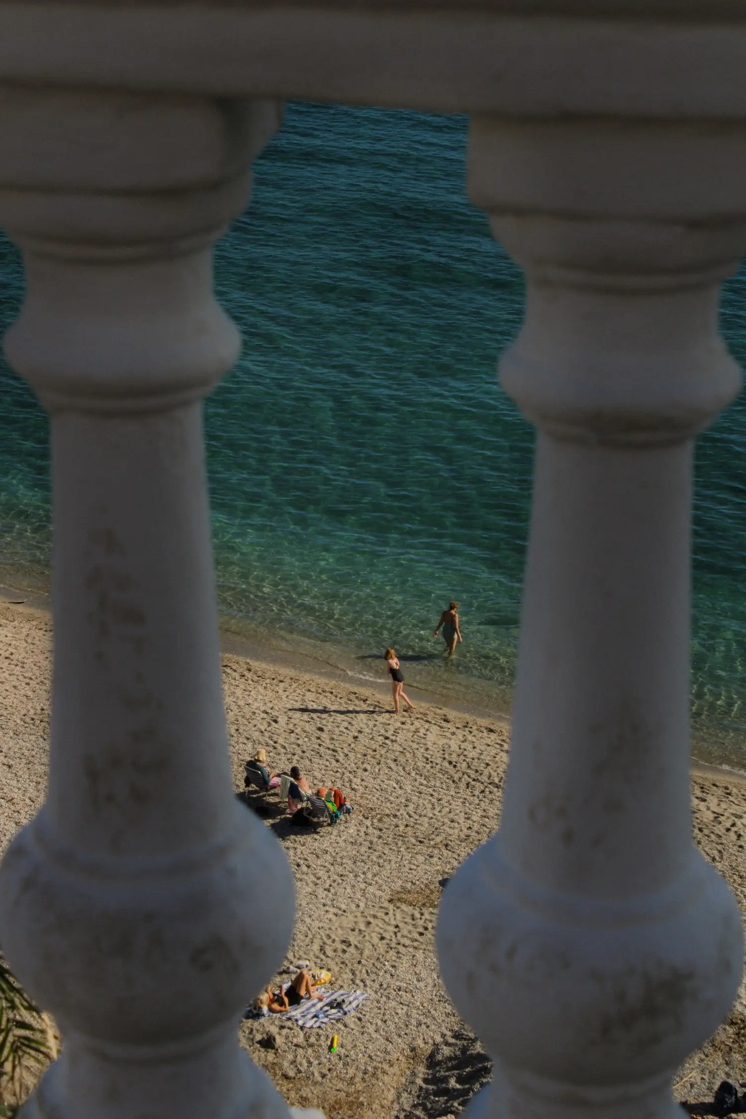 Perspectiva entre vallas blancas de cemento de una playa concurrida con bañistas disfrutando del mar